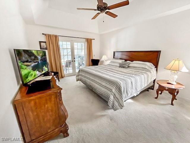 bedroom featuring french doors, light carpet, access to outside, a tray ceiling, and ceiling fan