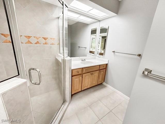 bathroom with a shower with door, vanity, tile patterned flooring, and a skylight