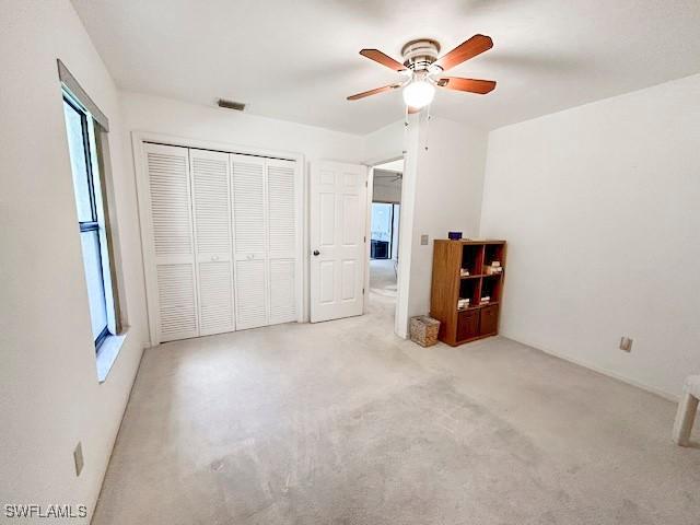 unfurnished bedroom featuring ceiling fan, a closet, light carpet, and multiple windows