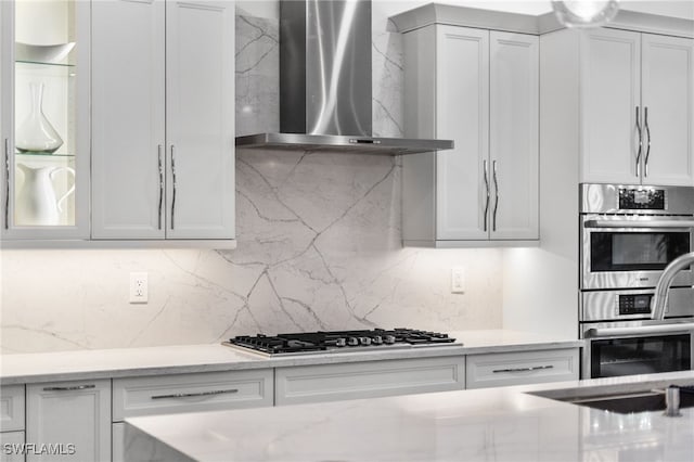 kitchen featuring tasteful backsplash, sink, light stone counters, stainless steel appliances, and wall chimney exhaust hood