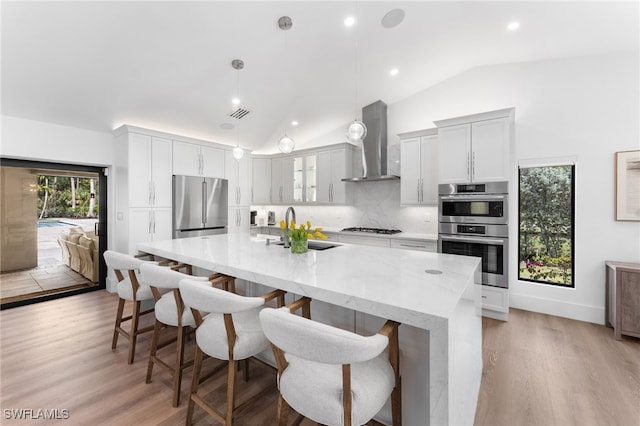 kitchen with wall chimney range hood, a breakfast bar, appliances with stainless steel finishes, a spacious island, and decorative light fixtures