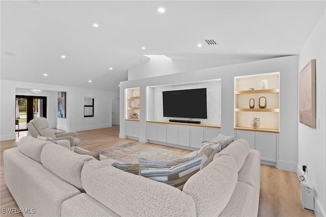 living room with built in shelves, light hardwood / wood-style flooring, and vaulted ceiling