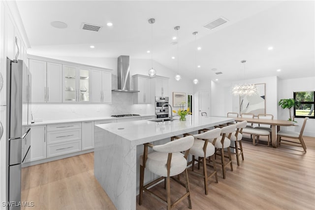 kitchen featuring hanging light fixtures, a breakfast bar area, wall chimney exhaust hood, and a center island with sink