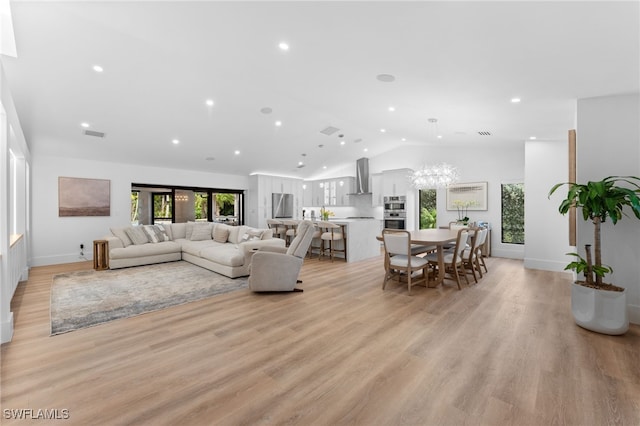 living room with vaulted ceiling, a notable chandelier, and light wood-type flooring