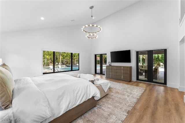 bedroom with an inviting chandelier, high vaulted ceiling, light hardwood / wood-style floors, access to outside, and french doors