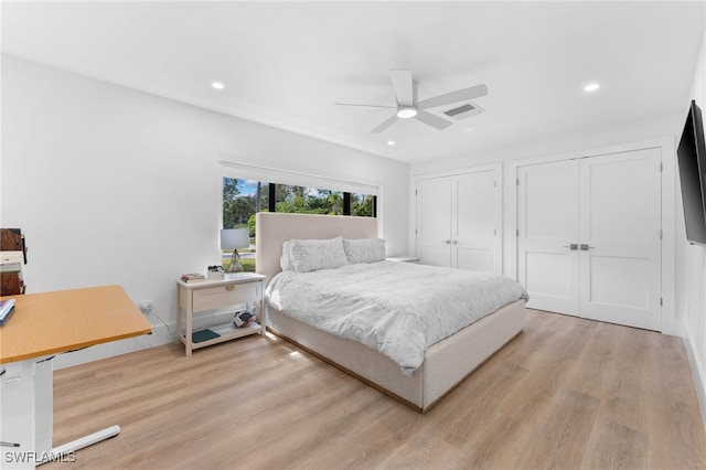 bedroom with ceiling fan, two closets, and light hardwood / wood-style floors