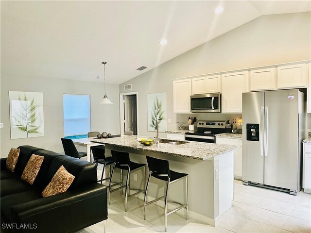 kitchen featuring hanging light fixtures, appliances with stainless steel finishes, a kitchen island with sink, white cabinets, and a kitchen bar