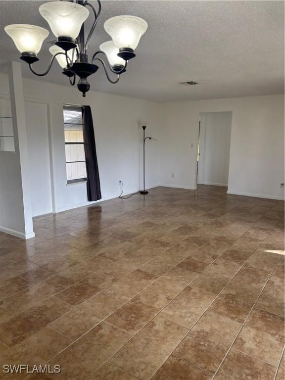 tiled empty room featuring a textured ceiling and a notable chandelier