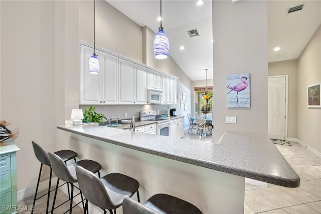 kitchen featuring white appliances, a breakfast bar, hanging light fixtures, white cabinets, and kitchen peninsula