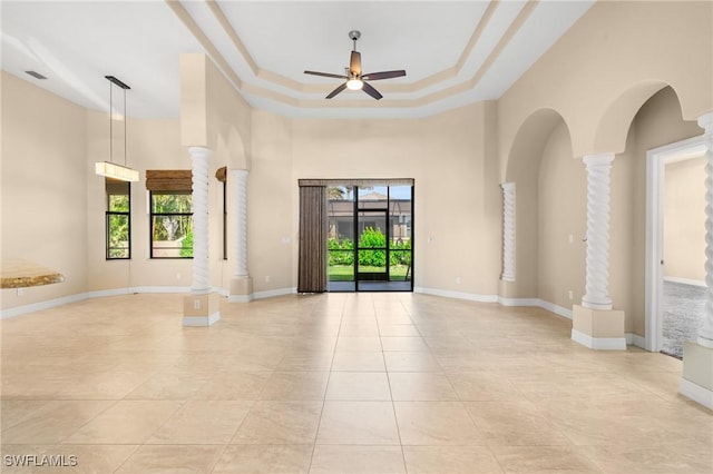 tiled empty room featuring decorative columns, a towering ceiling, ceiling fan, and a raised ceiling