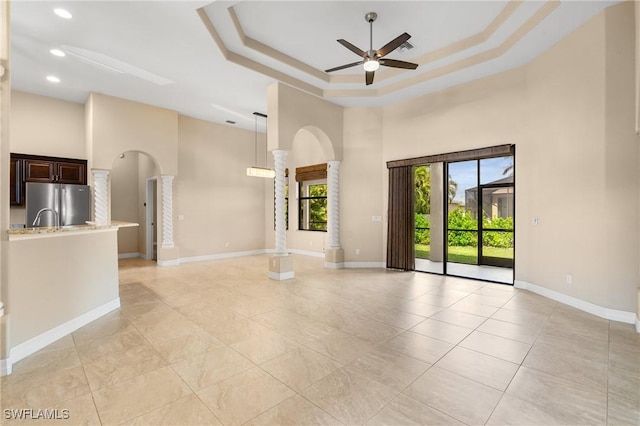 unfurnished living room with a tray ceiling, ceiling fan, decorative columns, and a towering ceiling