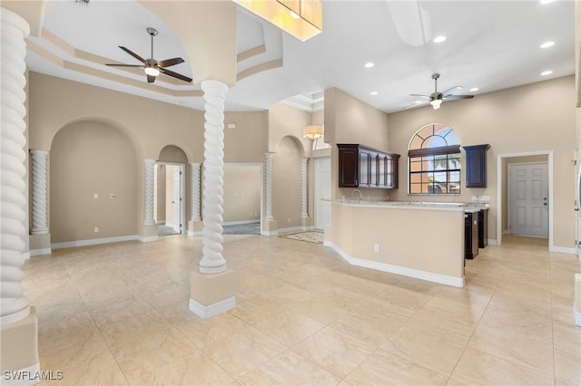 kitchen featuring dark brown cabinetry, a towering ceiling, ceiling fan, a tray ceiling, and decorative columns