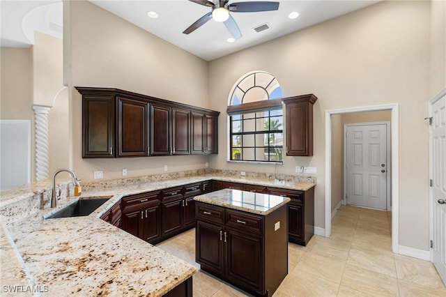 kitchen with dark brown cabinets, sink, light stone countertops, and kitchen peninsula