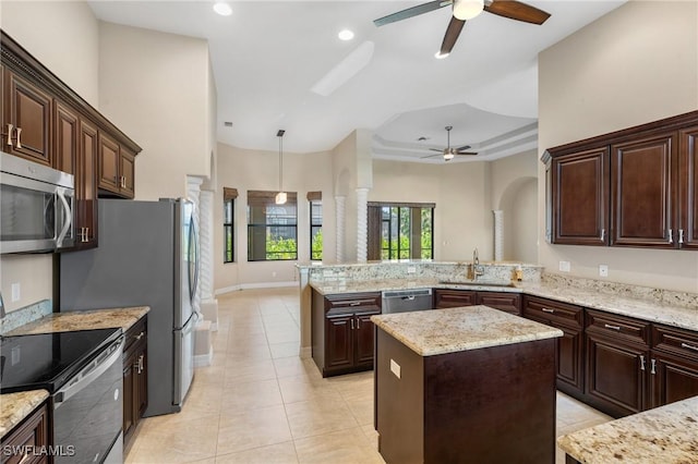 kitchen with appliances with stainless steel finishes, light stone counters, dark brown cabinetry, a center island, and kitchen peninsula