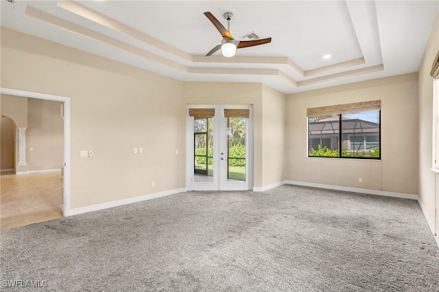 empty room with french doors, light colored carpet, plenty of natural light, and a raised ceiling