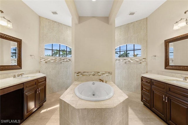 bathroom with tiled bath, a healthy amount of sunlight, tile patterned flooring, and vanity