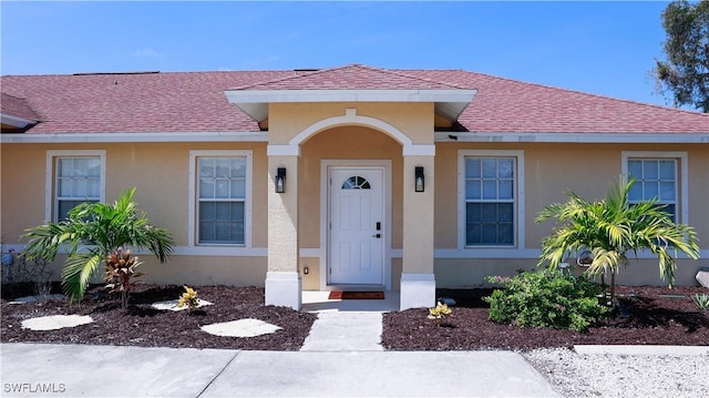 doorway to property with stucco siding and roof with shingles