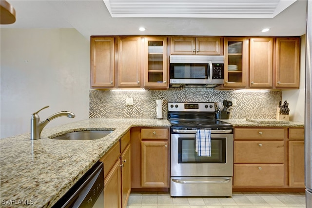 kitchen with sink, stainless steel appliances, a tray ceiling, light stone countertops, and decorative backsplash