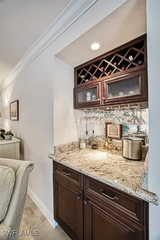 bar with ornamental molding, light stone countertops, and dark brown cabinets