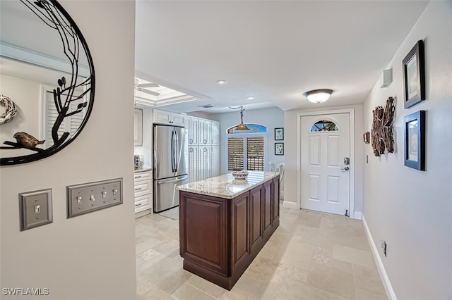 kitchen with stainless steel refrigerator, dark brown cabinets, a center island, and light stone counters