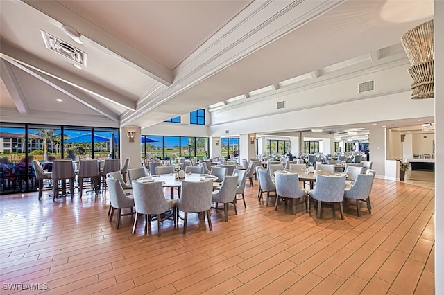 dining area featuring beam ceiling, a high ceiling, and light wood-type flooring