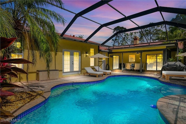 pool at dusk with an outdoor pool, a patio, glass enclosure, grilling area, and french doors