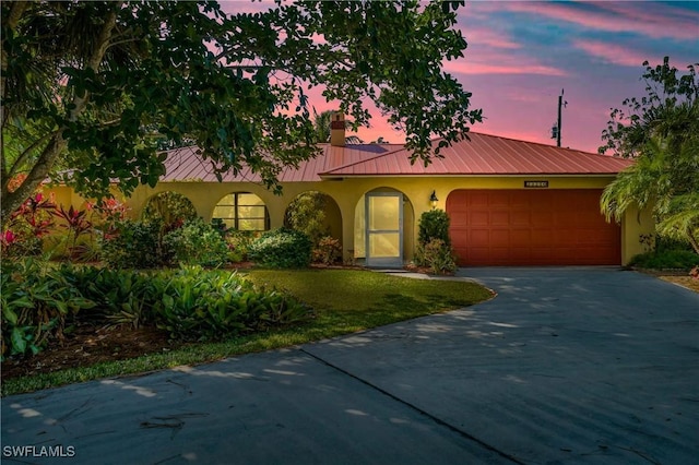 mediterranean / spanish-style house featuring a garage, driveway, metal roof, and stucco siding