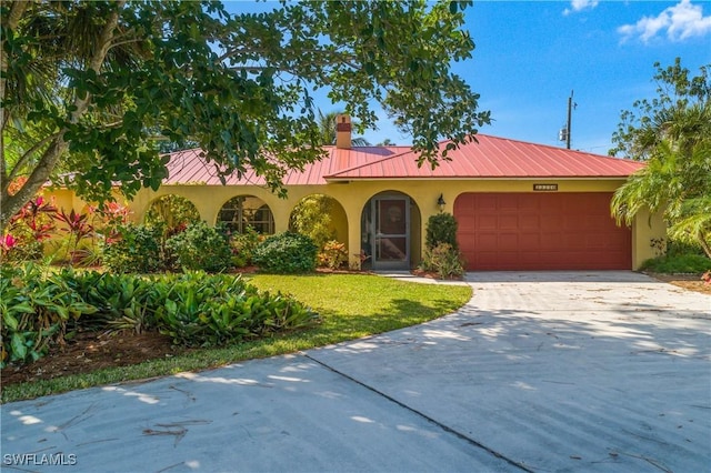 mediterranean / spanish house with stucco siding, concrete driveway, a front yard, metal roof, and a garage