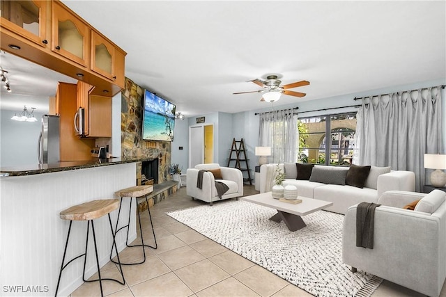 living area featuring ceiling fan, a stone fireplace, and light tile patterned floors