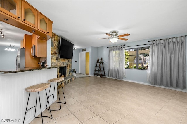 kitchen featuring stainless steel appliances, a ceiling fan, brown cabinetry, a kitchen bar, and glass insert cabinets