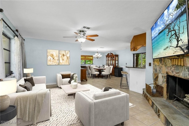 living area with light tile patterned floors, baseboards, visible vents, a fireplace, and ceiling fan with notable chandelier