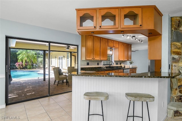 kitchen with light tile patterned floors, glass insert cabinets, dark stone counters, and a sink