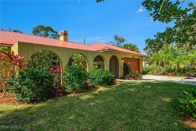 mediterranean / spanish-style house with a chimney, stucco siding, a front yard, a garage, and driveway