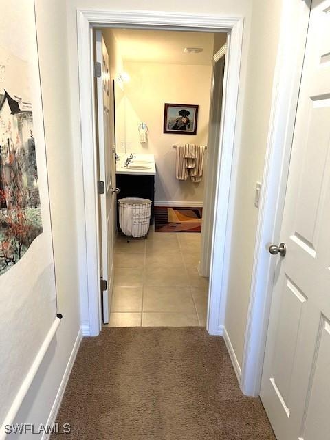 corridor with light tile patterned floors, light carpet, baseboards, and a sink