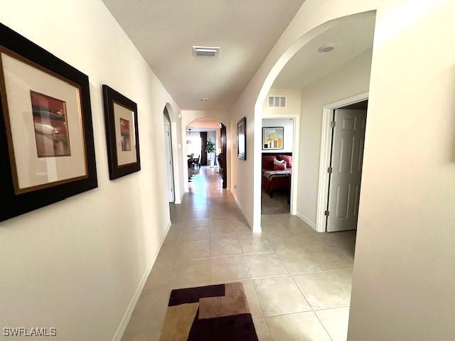 hall with light tile patterned floors, visible vents, arched walkways, and baseboards