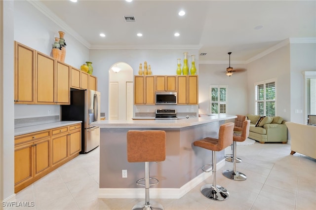 kitchen with appliances with stainless steel finishes, a kitchen bar, light tile patterned flooring, light countertops, and crown molding