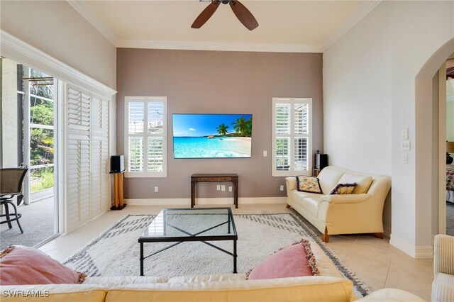 living room with arched walkways, tile patterned flooring, crown molding, ceiling fan, and baseboards
