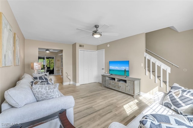 living room with light wood finished floors, visible vents, baseboards, a ceiling fan, and stairway