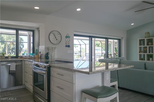 kitchen featuring light stone counters, kitchen peninsula, stainless steel appliances, hardwood / wood-style floors, and white cabinets