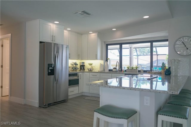 kitchen featuring a kitchen bar, white cabinetry, light stone counters, appliances with stainless steel finishes, and kitchen peninsula