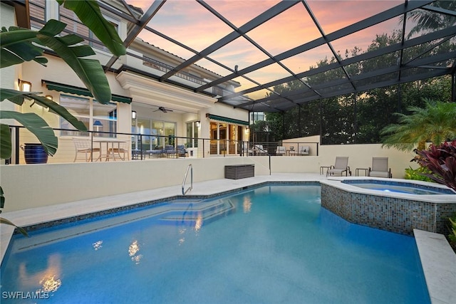 pool at dusk featuring an in ground hot tub, ceiling fan, a lanai, and a patio