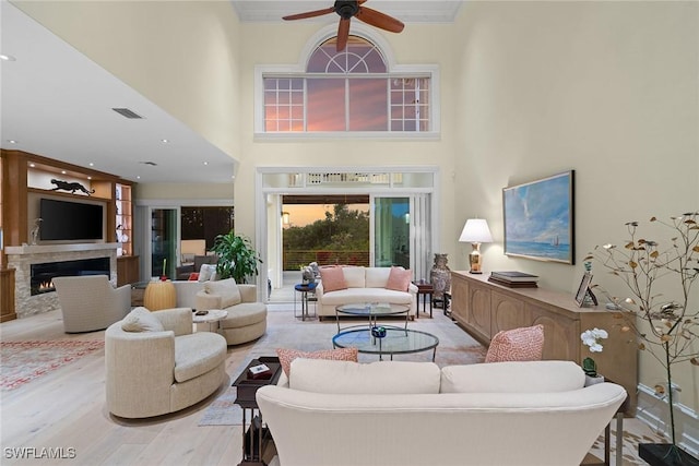 living room featuring ceiling fan, a towering ceiling, and light wood-type flooring