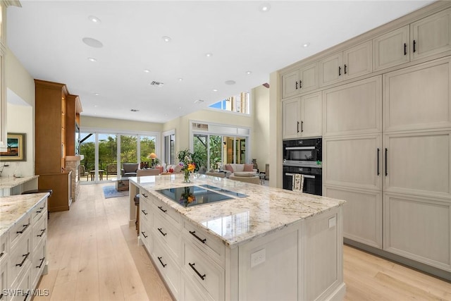 kitchen featuring a kitchen island, light stone counters, black electric cooktop, and light hardwood / wood-style floors