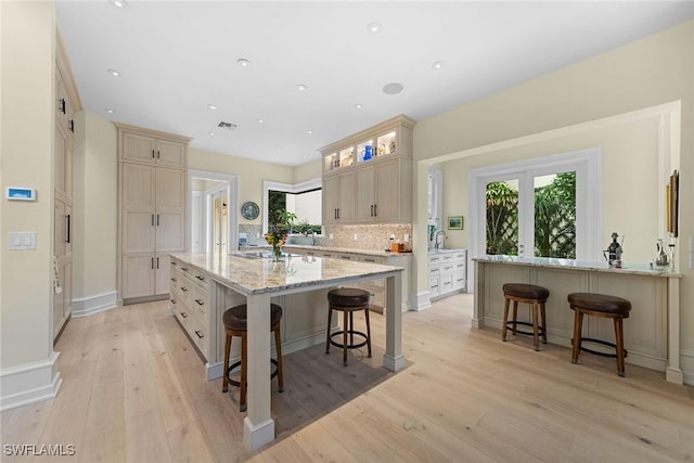 kitchen with a kitchen breakfast bar, light stone counters, tasteful backsplash, a large island with sink, and light wood-type flooring