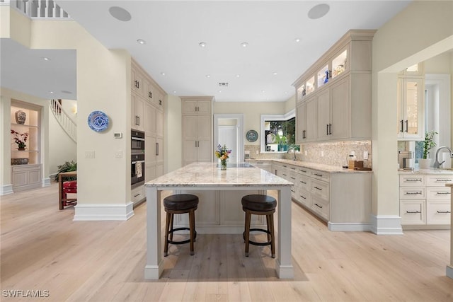 kitchen with a kitchen island, a breakfast bar, backsplash, light stone countertops, and light hardwood / wood-style flooring