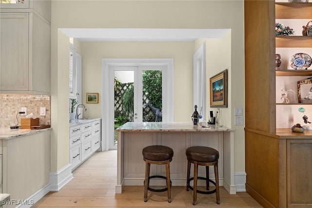 bar featuring sink, light stone counters, light hardwood / wood-style floors, decorative backsplash, and white cabinets