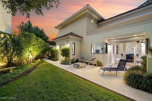 back house at dusk with a patio area and a lawn