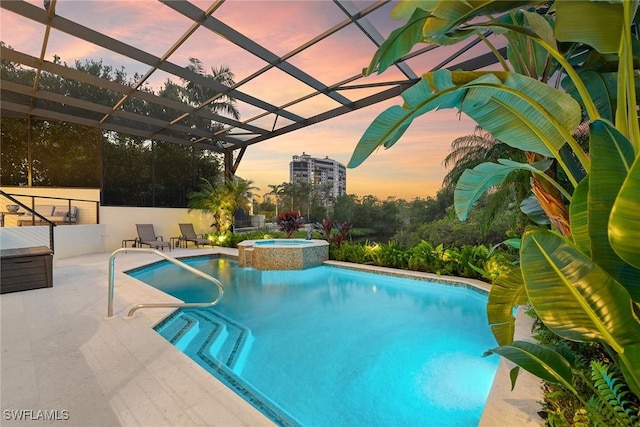 pool at dusk with a lanai, a patio, and an in ground hot tub