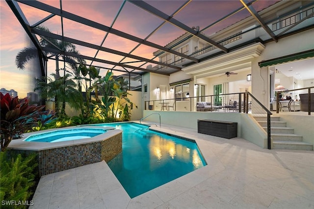 pool at dusk with an in ground hot tub, ceiling fan, a patio, and glass enclosure