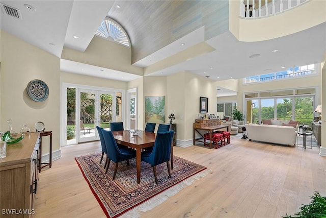 dining space featuring french doors, a towering ceiling, and light hardwood / wood-style flooring